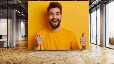 Young handsome man with beard over isolated yellow background with thumbs up because something good has happened. Wall mural