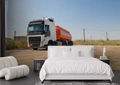 A truck with an orange tank goes on a knurled unpaved road Wall mural