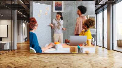 Asian business woman having presentation on white board with African-American colleague in front of other two coworkers. Wall mural