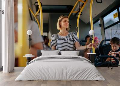 Group of people commuting by bus. The focus is on the young woman with suitcase holding the railing. Wall mural