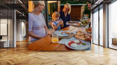 Happy family having fun together in the backyard. Little girl, her mother and grandmother at the dining table Wall mural