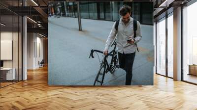 Stylish young man standing outside with his bicycle and using phone Wall mural