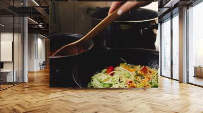 Cooking tomatoes, grated carrot and zucchini on a pan, female hands, closed view Wall mural