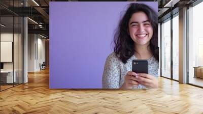 young smiling woman using mobile phone against purple background Wall mural