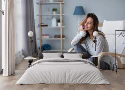 Beautiful happy woman looking at camera and smiling while sitting in a cozy chair. Wall mural