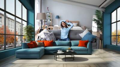 Happy casual beautiful woman sitting on a sofa at home. Wall mural