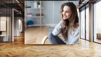 Happy woman posing sitting on a sofa in the living room at home. Wall mural