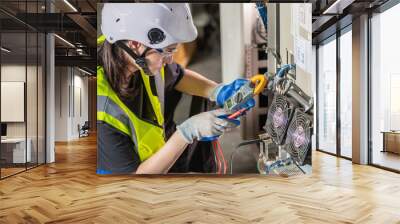 Woman Electrician engineer work check tester measuring voltage and current of power electric line in electricity cabinet control. Workers use clamp meter to measure current electrical wires Wall mural