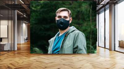 Caucasian man in black protective mask outside. Guy portrait in medical mask on forest landscape alone keeping social distancing. Protection against coronavirus, epidemic covid 19, smog air pollution Wall mural