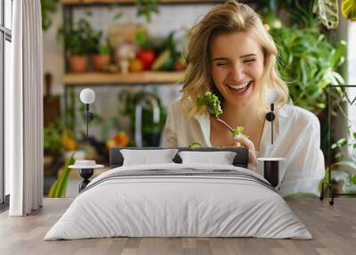 A joyful woman enjoying a fresh salad in a bright kitchen filled with green plants, emphasizing healthy eating and a happy lifestyle. Wall mural