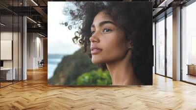 A woman with curly hair standing by the sea, representing natural beauty, reflection, and connection with nature. Wall mural