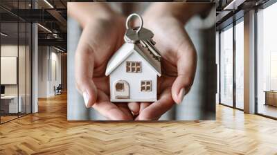 Hands holding a small house model with keys, symbolizing real estate ownership and home security, evoking a sense of trust and stability. Wall mural