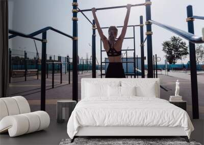 young woman in sportswear doing chin ups exercises at outdoor workout station Wall mural