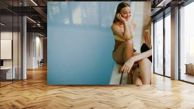 Beautiful young women sitting by the indoor swimming pool Wall mural