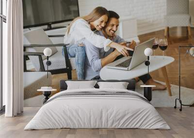 Cheerful couple searching internet on laptop at home Wall mural