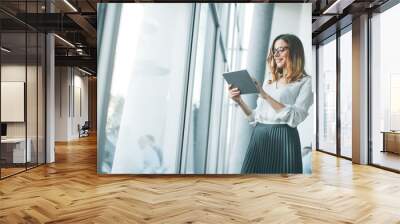 Elegant businesswoman standing in office with digital tablet Wall mural