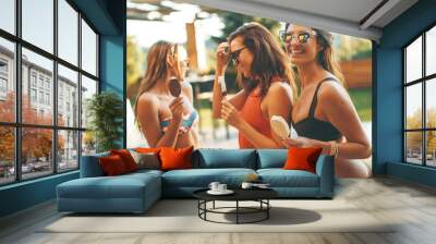 Female friends eating icecream by pool in summer Wall mural