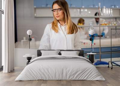 Female researcher in white lab coat and protective mask using laptop while working in the lab Wall mural