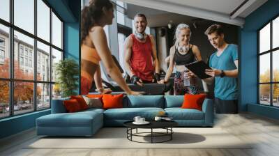 Friends in sportswear talking and laughing together while resting in the gym after a workout Wall mural