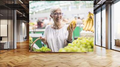 Good-looking senior woman buys bananas at the market Wall mural