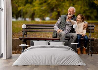 Grandfather spending time with his granddaughter on bench in park on autumn day Wall mural