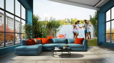 Group of friends with cider bottles standing by the boat near the beautiful lake and having fun Wall mural