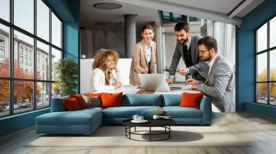 Group of young business people working and communicating while sitting at the office desk together Wall mural