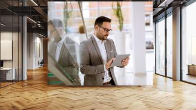 Happy businessman dressed in suit standing  in modern office  and using tablet Wall mural