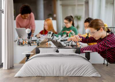 Happy kids with their African American female science teacher with laptop programming electric toys and robots at robotics classroom Wall mural