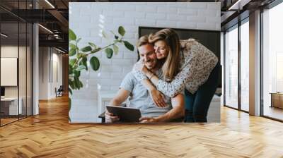 Happy young couple looking at digital tablet in living room Wall mural