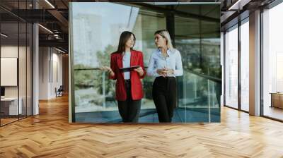 Two businesswomen discuss strategy outside modern office building in daylight Wall mural