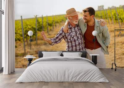 Two men stroll through a sunlit vineyard, sharing laughter and stories on a warm afternoon, surrounded by lush green vines Wall mural