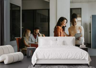 Two young business women with digital tablet in the office in front of their team Wall mural