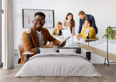 Young African American business man working with digital tablet in front of his coworkers at boardroom Wall mural