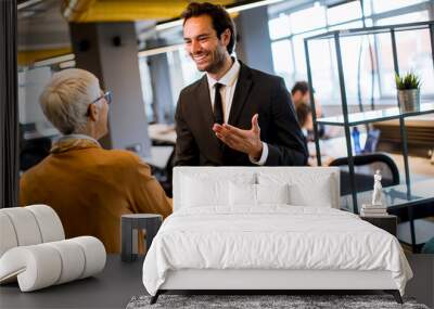 Young business man and senior business woman shaking hands in the office Wall mural