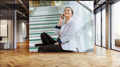 Young business woman sitting on the stairs at the office and use mobile phone Wall mural