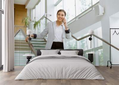 Young business woman stands on the stairs at the office and use mobile phone Wall mural