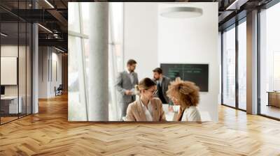 young businesswomen discussing with digital tablet in the office with young people works behind them Wall mural