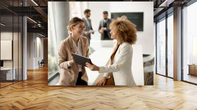 Young businesswomen discussing with digital tablet in the office with young people works behind them Wall mural