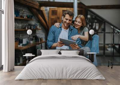 Young couple is using a digital tablet and smiling in kitchen at home Wall mural