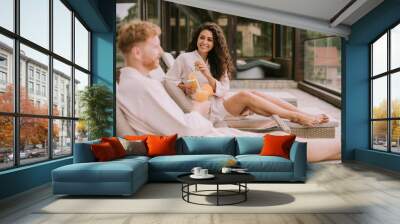 Young couple relaxing on beds and drinking fresh orange juice on the outdoor terrace Wall mural