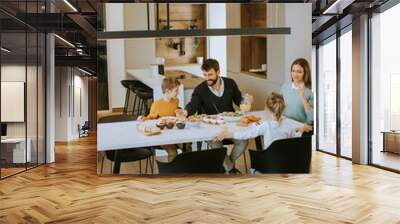 Young happy family talking while having lunch at dining table Wall mural