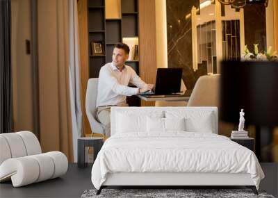 Young man sitting in a luxurious room in front of a laptop computer Wall mural