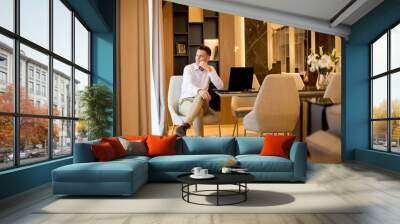 Young man sitting in a luxurious room in front of a laptop computer Wall mural