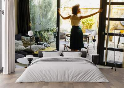 Young woman with curly hair standing in the house next to the open glass door Wall mural