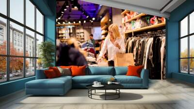 Young woman with shopping bags standing at the clothing store Wall mural