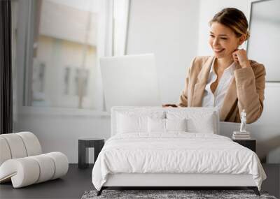 Young woman working on laptop in bright office with big screen behind her Wall mural