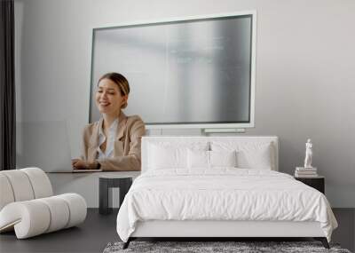 Young woman working on laptop in bright office with big screen behind her Wall mural