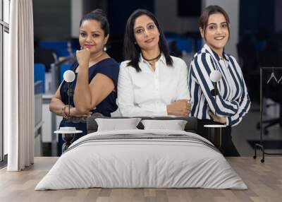 Three Indian businesswomen with arms folded standing together against office background, corporate environment. Wall mural