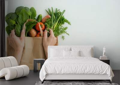 The photo shows a brown supermarket paper bag containing vegetablesheld by two hands and dumped on a white table topwas shot from top angle Space for advertising Wall mural